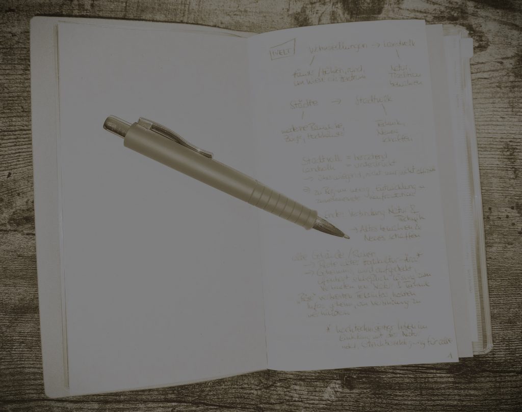 Die Schritte vor dem Plotten veranschaulicht anhand eines aufgeschlagenen Notizbuchs und eines daraufliegenden Stifts